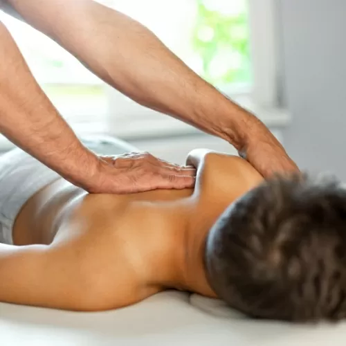 Hands performing soft tissue therapy on a patient's upper back